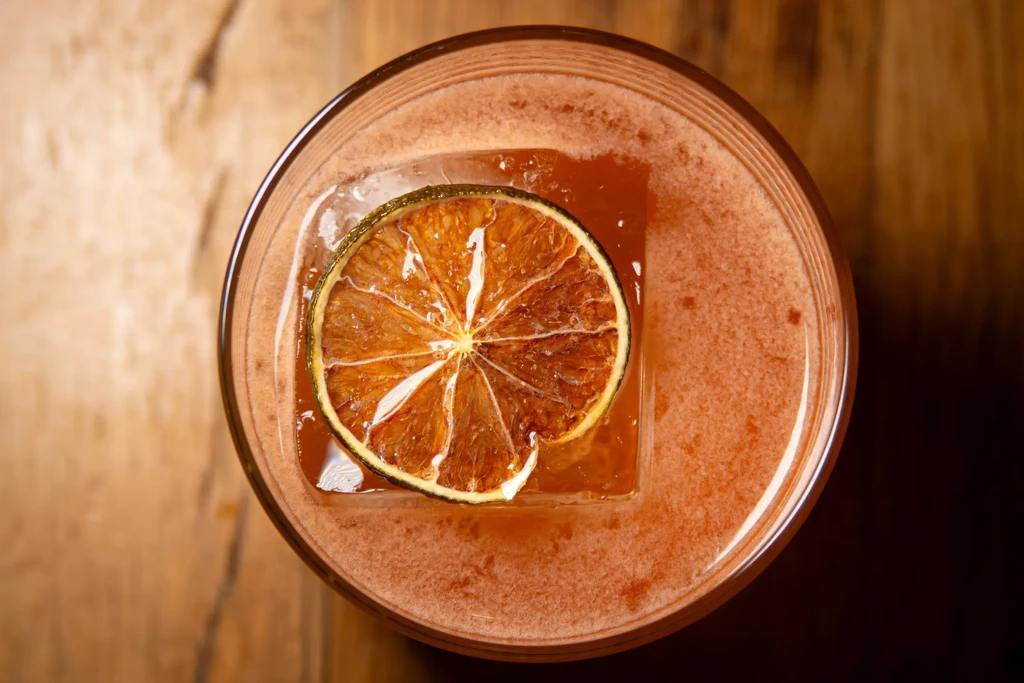 Overhead shot of a reddish-orange cocktail with citrus on ice.