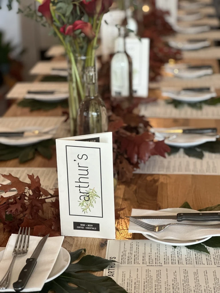 Restaurant table with "arthur's" menu, place settings, and autumn leaf decor.