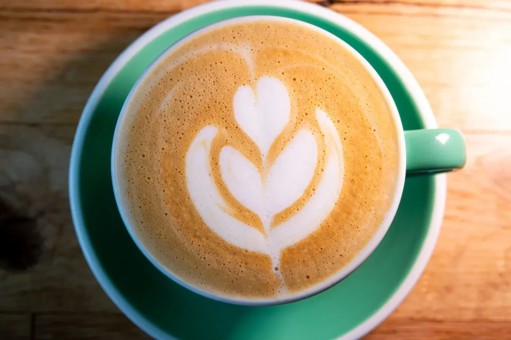 White foamed heart art in a teal ceramic coffee cup.