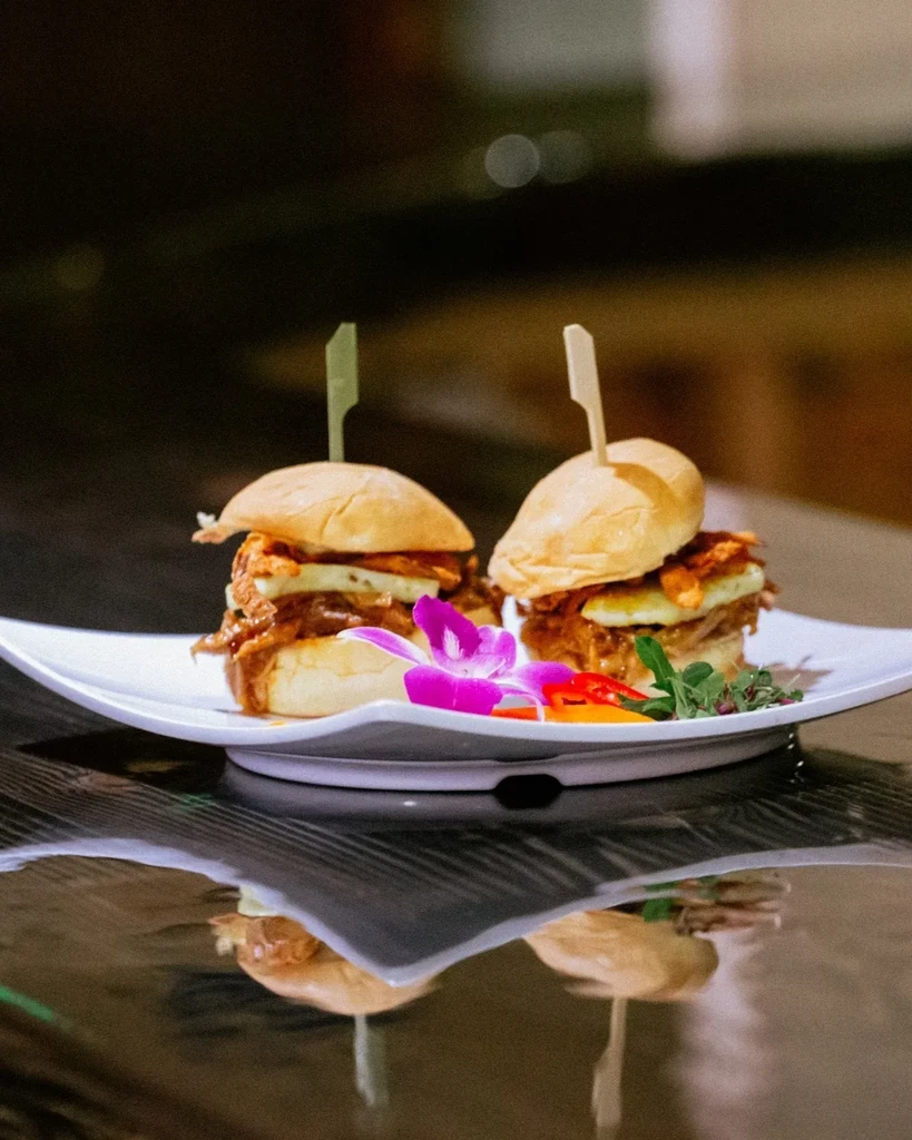 Two pulled meat and fried egg sliders, garnished with orchid and peppers.