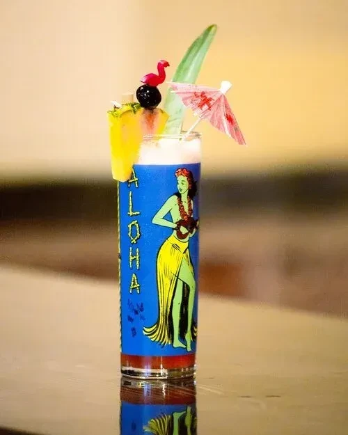 Layered blue cocktail in an ALOHA glass with pineapple and umbrella.