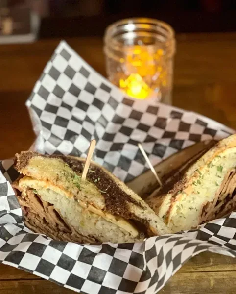 Layered deli sandwich on marbled rye, in basket, warm light.