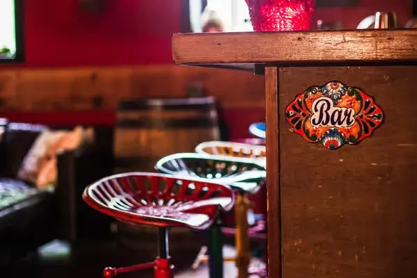 Warm, rustic bar with ornate 'Bar' sign and red tractor-seat stools.