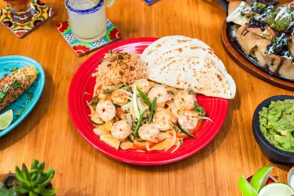 Mexican-inspired shrimp meal, elote, guacamole, and drinks on a wooden table.