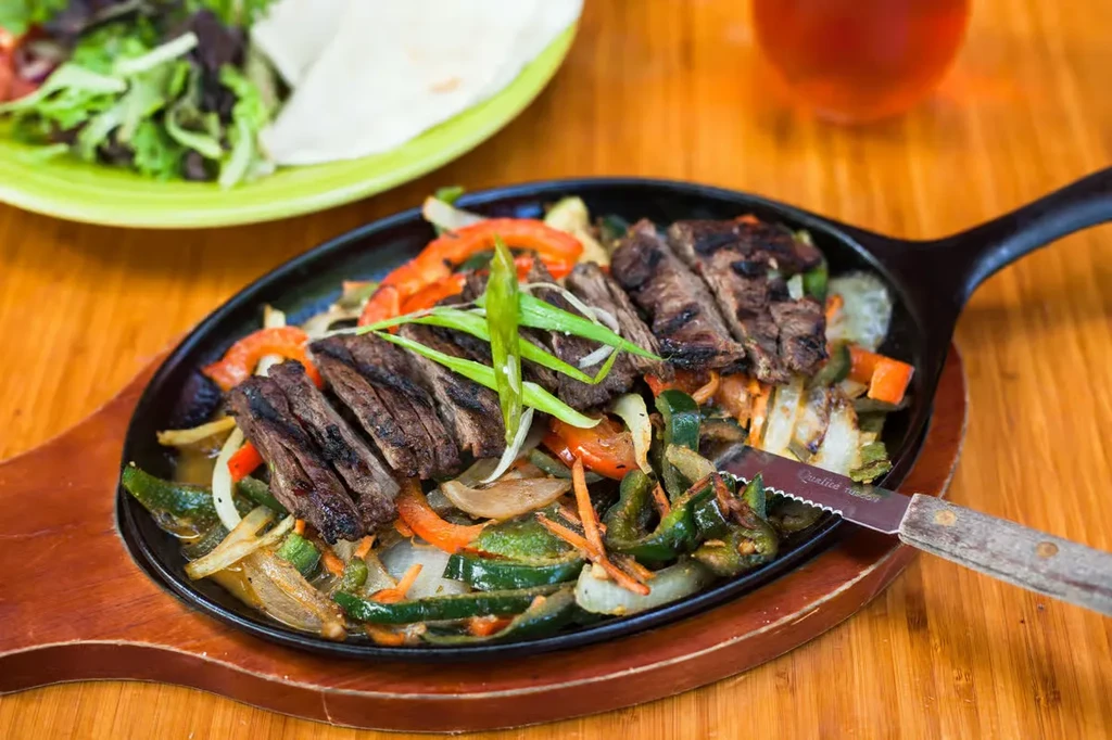 Close-up of vibrant, sizzling steak fajitas in a cast iron skillet.