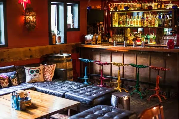 Cozy bar interior with a sofa, stocked bar, and colorful stools.