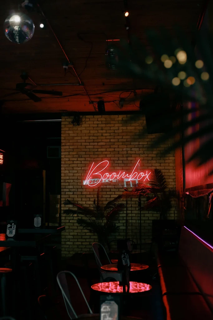 Dark bar interior with 'Boombox' neon sign, disco ball, red lighting.
