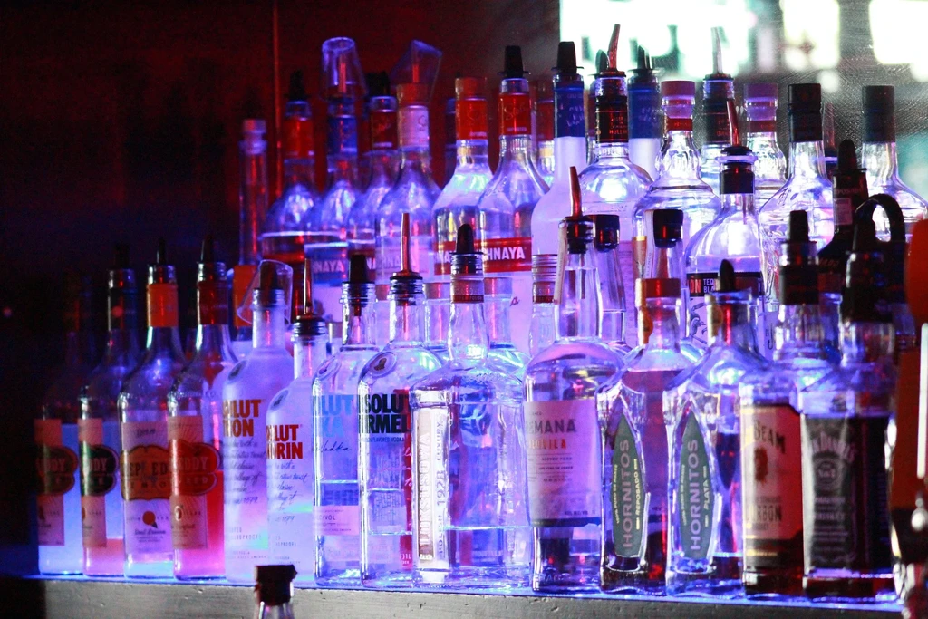 Numerous labeled liquor bottles with pourers glow on a bar shelf.