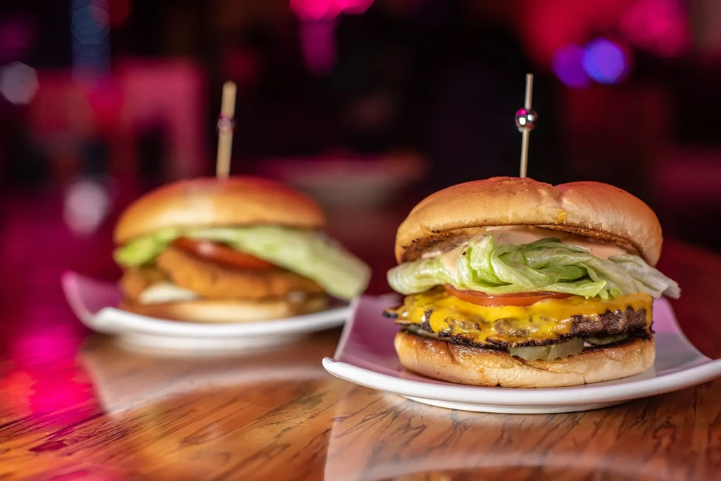 Sharply focused grilled burger with cheese, tomato, lettuce; another blurred.