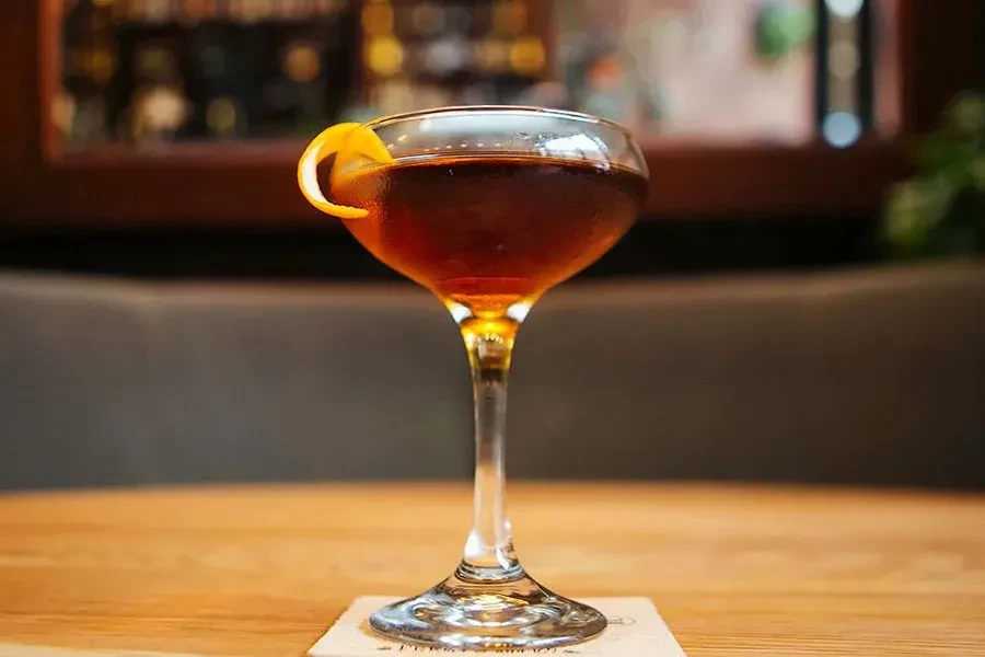 Dark amber cocktail in coupe glass, garnished with citrus peel.