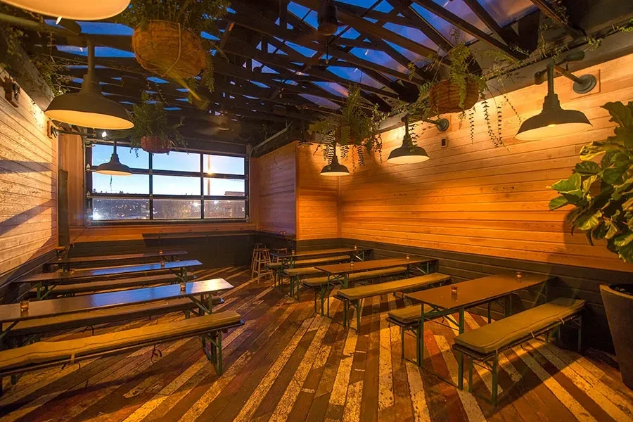 Empty rustic industrial restaurant with wooden tables, warm lighting, city view.