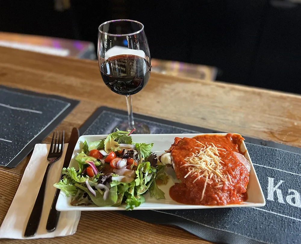 Chicken parmesan, green salad, and red wine on a wooden table.
