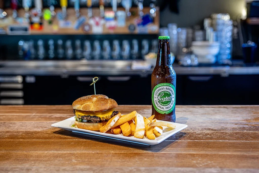 Cheeseburger, fries, and Coopers Pale Ale on a plate at a rustic bar.