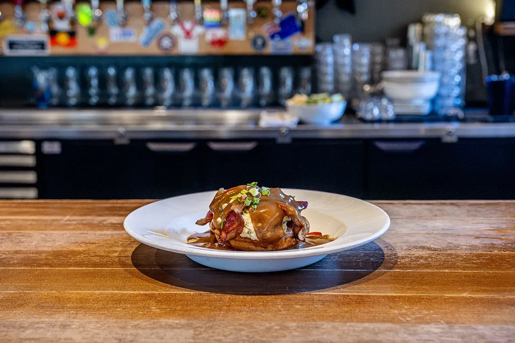 Savory dish with gravy, bacon, chives, blurred pub background.