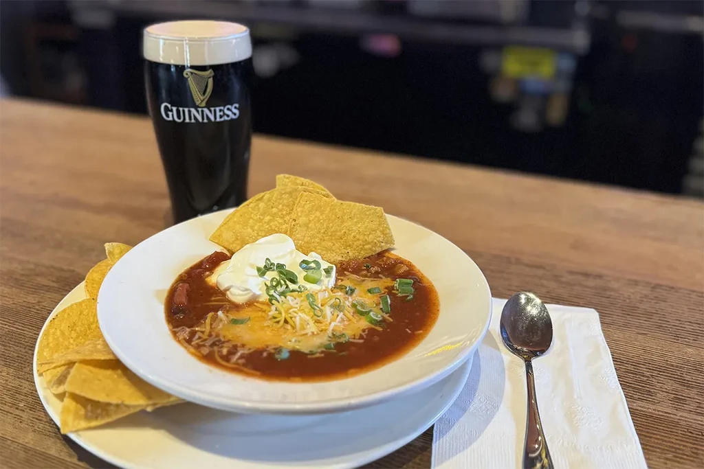 Chili with melted cheese, sour cream, tortilla chips, and Guinness pint.