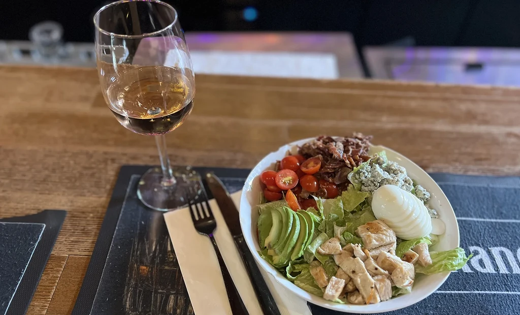 A Cobb-style salad with grilled chicken and white wine on a table.