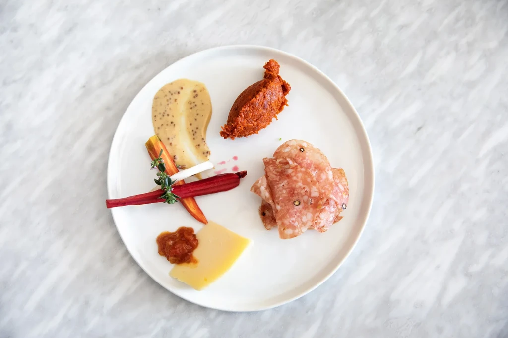 Appetizer plate with cured meat, cheese, spreads, and tied root vegetables.