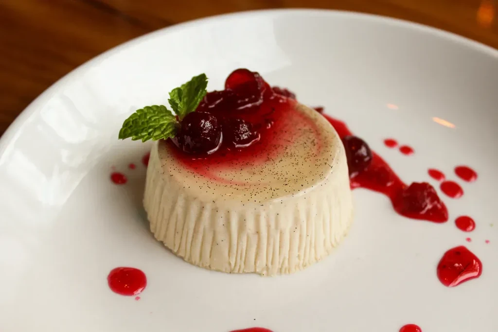 White plate with vanilla dessert, red berry sauce, cranberries, and mint.