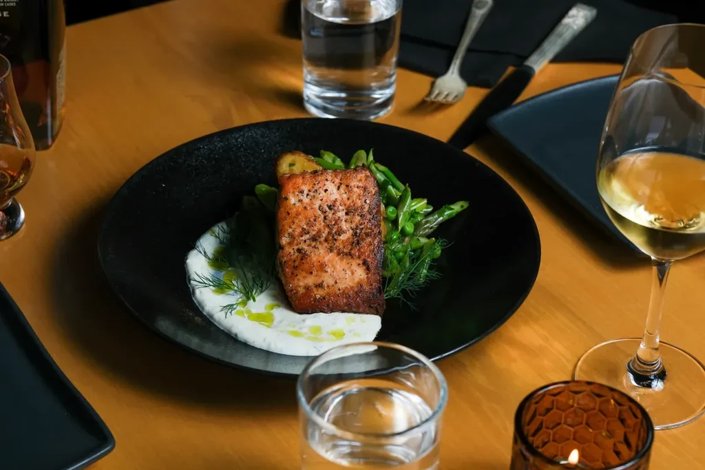 Neatly arranged salmon, vegetables, and wine on a warm wooden table.
