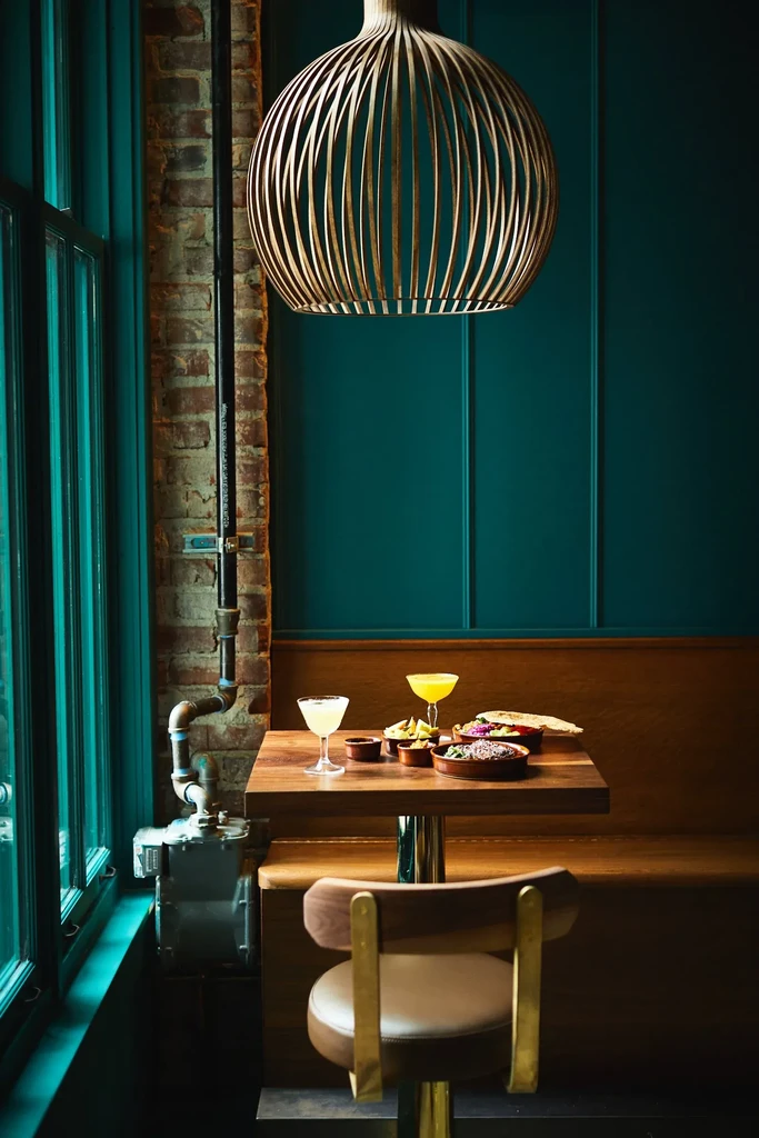 Restaurant interior with cocktails, appetizers, unique wooden light, teal, and brick.