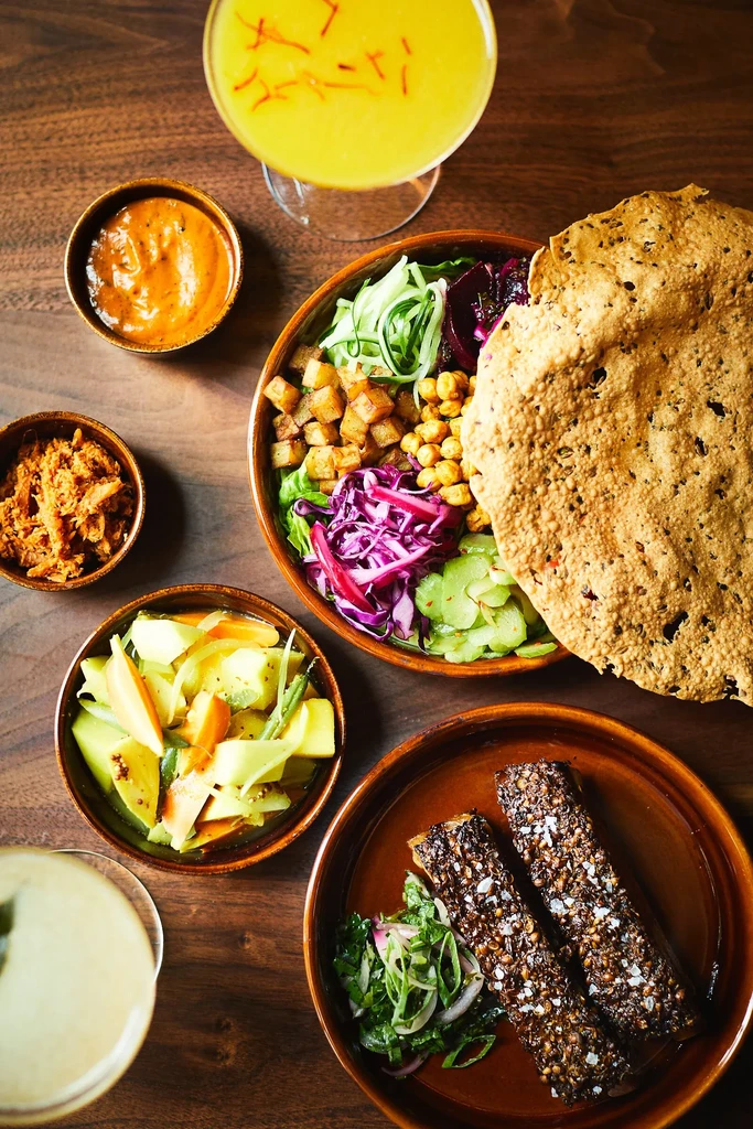 Colorful Indian salad bowl, accompaniments, and drinks on a wooden table.