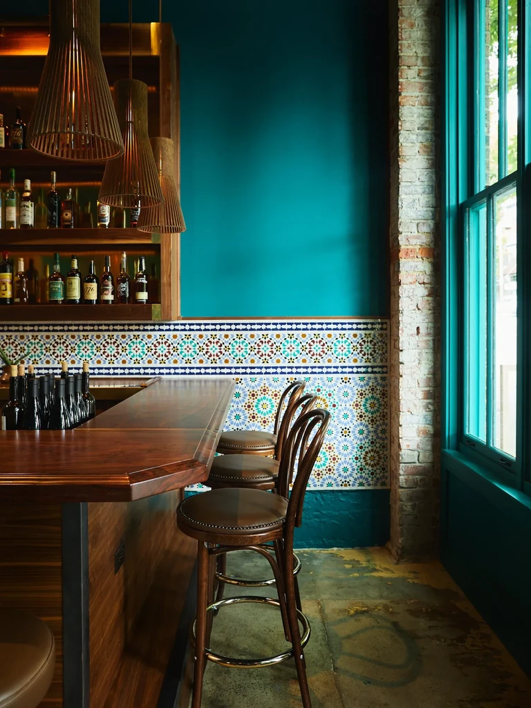 Empty bar with teal wall, Moorish tiles, and modern lighting.