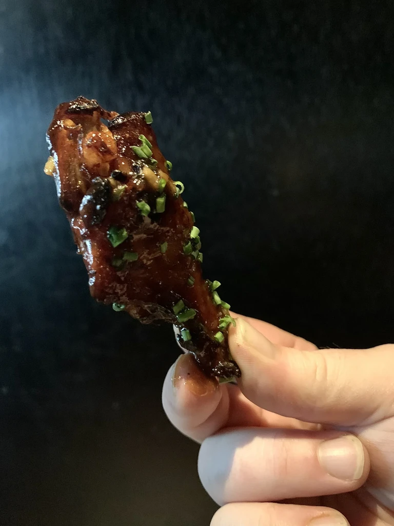 Glossy glazed chicken wing with green chives, held by a hand.