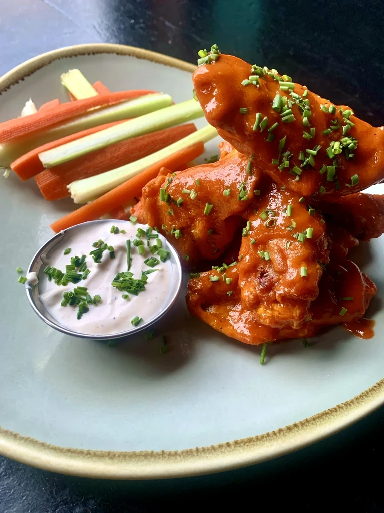Saucy chicken wings, vegetable sticks, and dip on a blue plate.