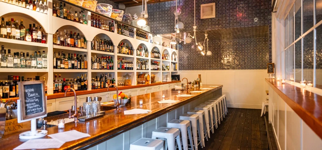 Sophisticated bar with long wooden counter, liquor bottles, and white barstools.
