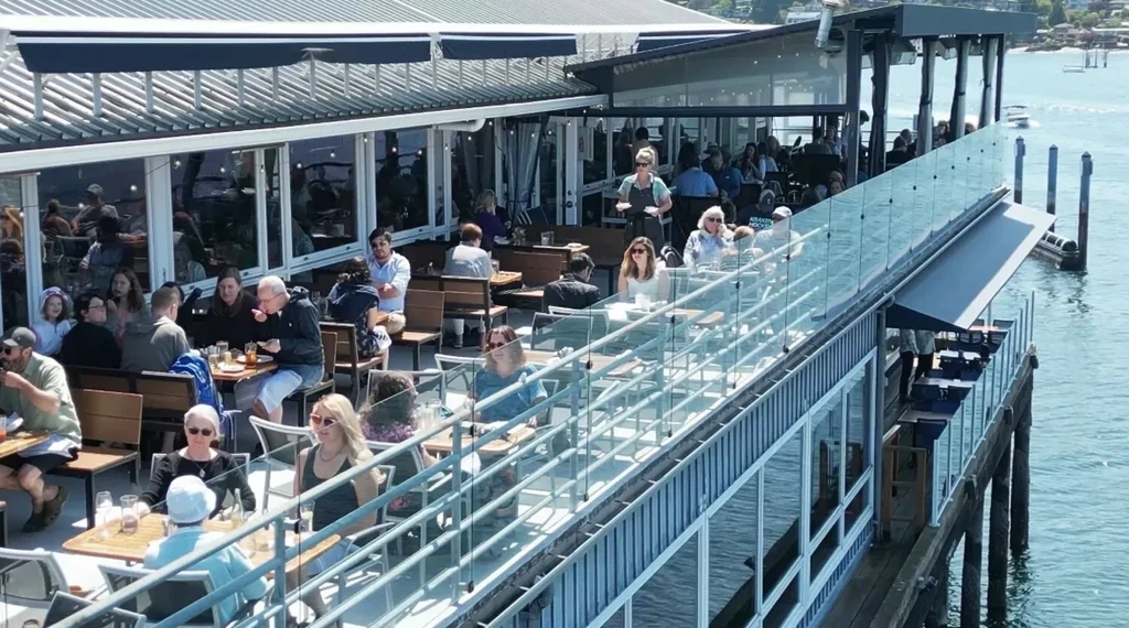 Sunny multi-level waterfront restaurant patio, busy with diners.