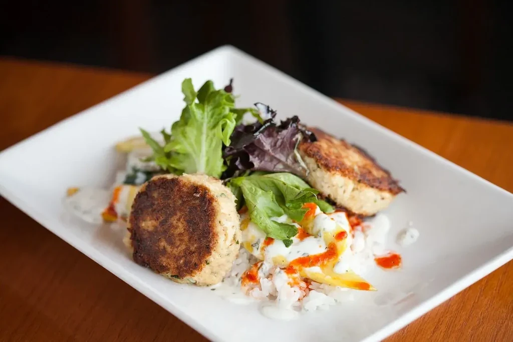 Two browned patties on rice with sauces and lettuce on a white plate.