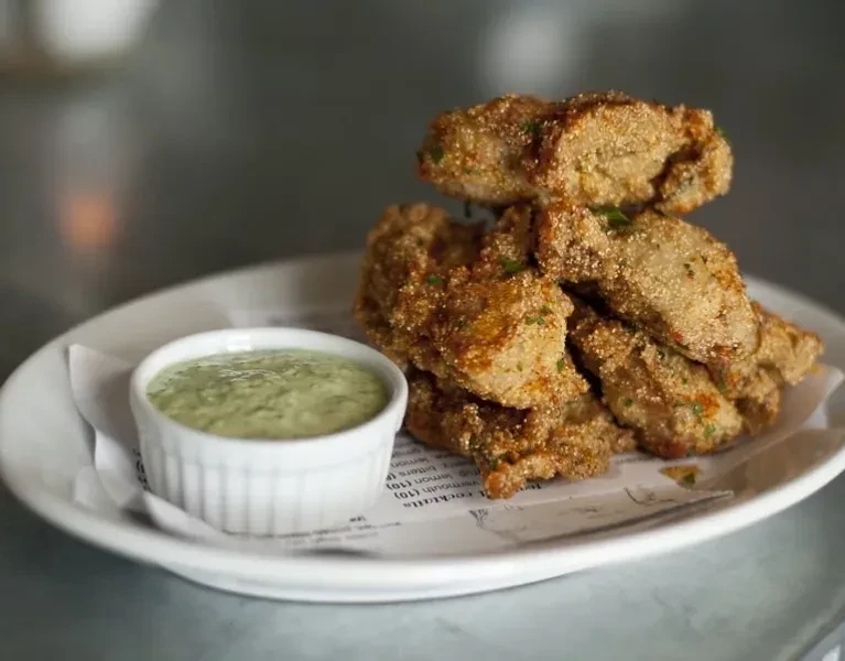 Golden-brown fried food pile, green herbs, and pale green dipping sauce.