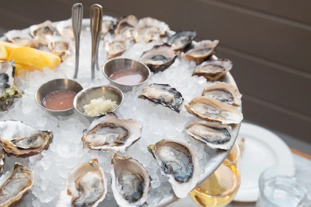 Fresh shucked oysters on ice with sauces, lemon, and forks.