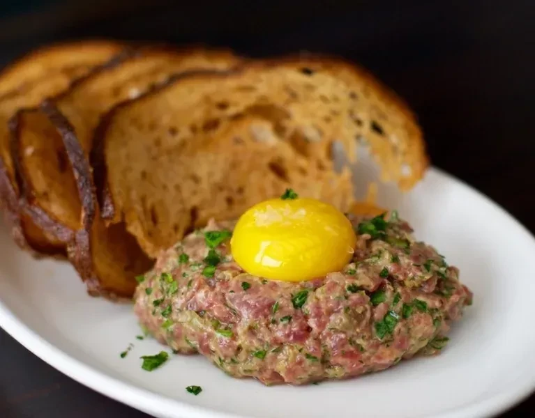 Steak tartare with egg yolk, green herbs, and toasted bread.