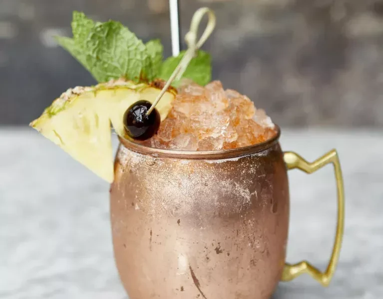 Cocktail in copper mug with crushed ice, mint, pineapple, and cherry.