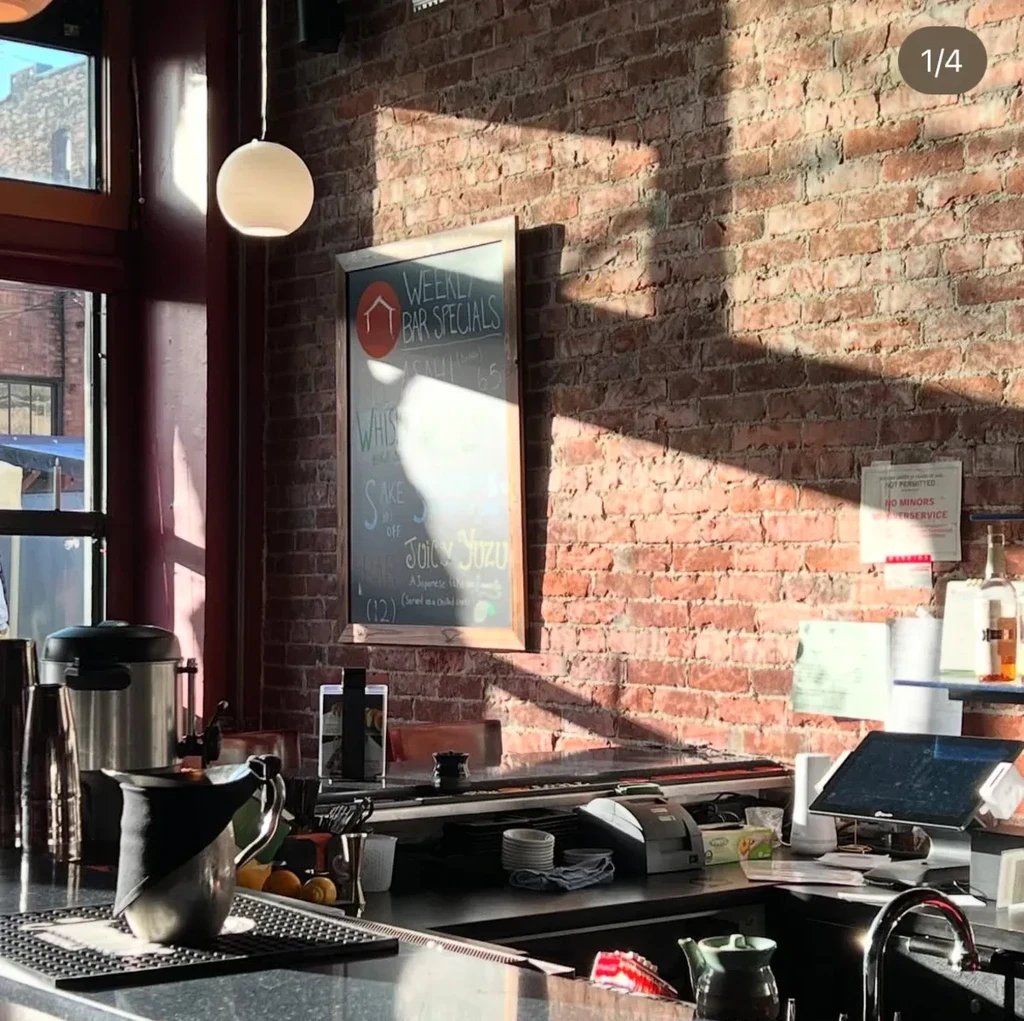 Sunlit bar interior with brick wall, counter, and weekly specials board.