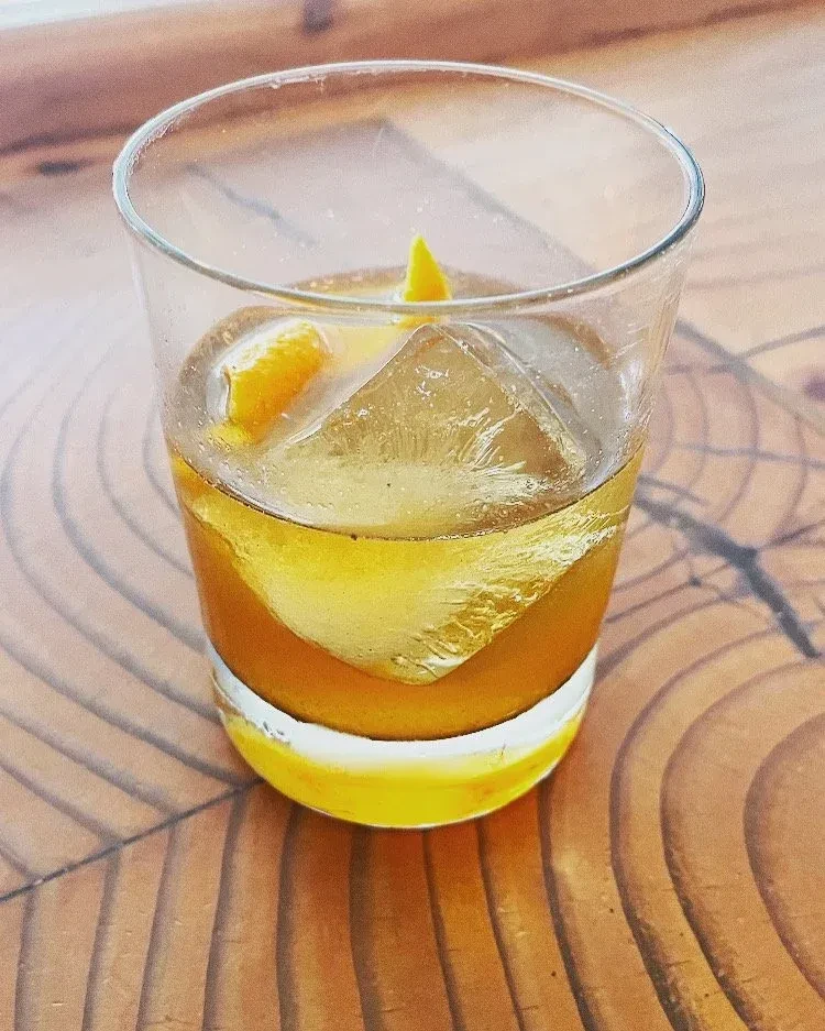 Amber cocktail in a short glass with square ice and citrus peels.