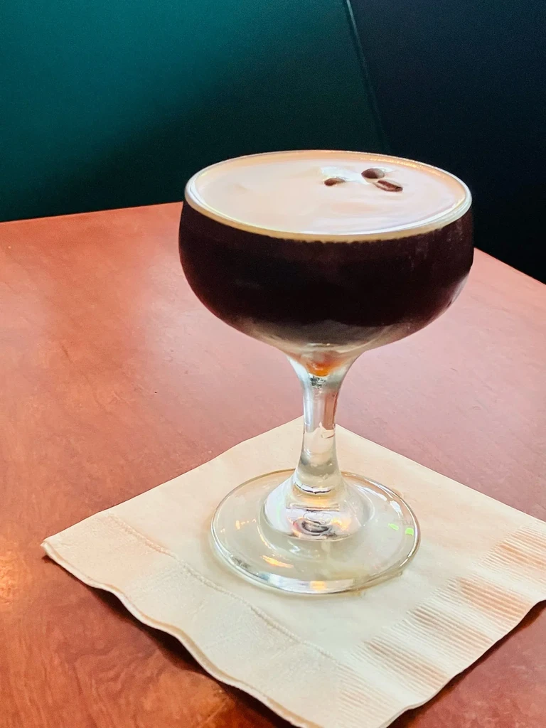 Espresso martini in coupe glass with foam, garnished with three coffee beans.