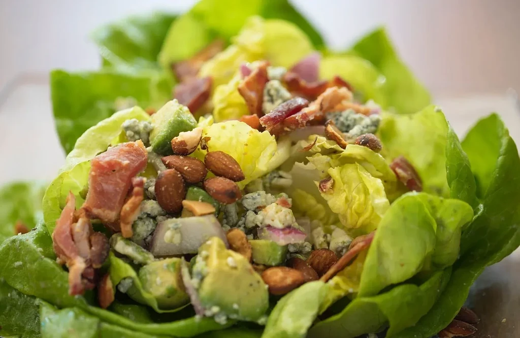 Vibrant salad with lettuce, avocado, blue cheese, bacon bits, and almonds.