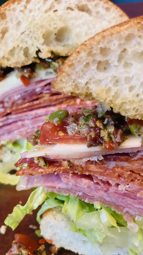 Halved sandwich with deli meats, cheese, tomato, lettuce, and olives.