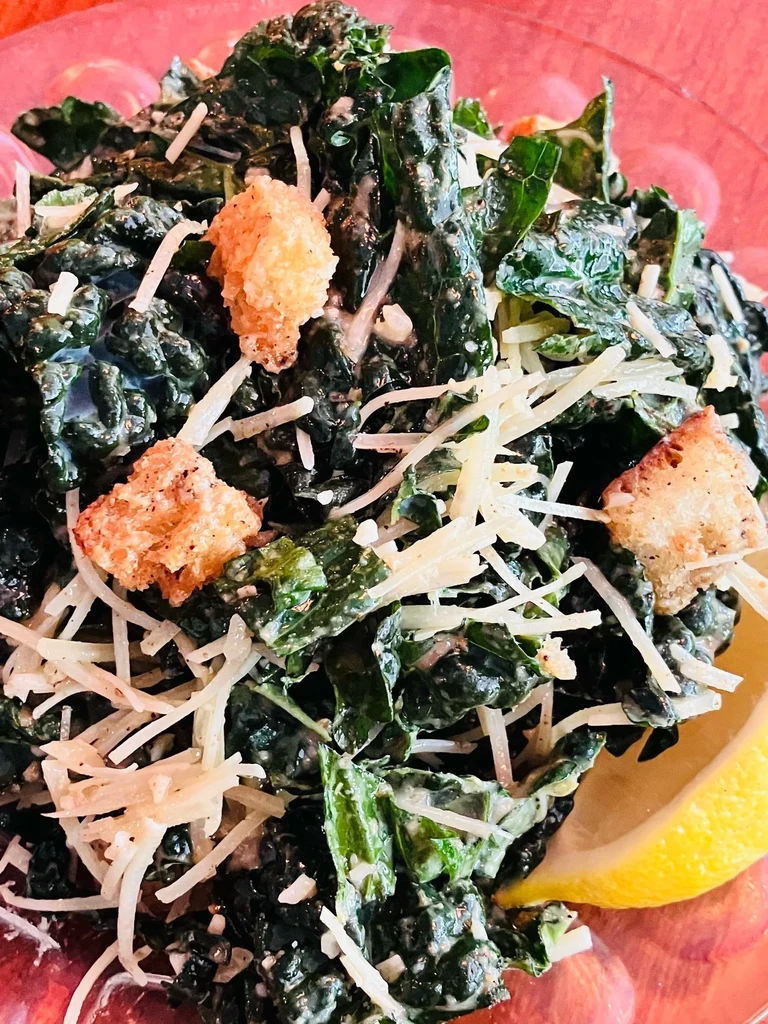 Vibrant kale salad with creamy dressing, shredded cheese, croutons, and lemon.