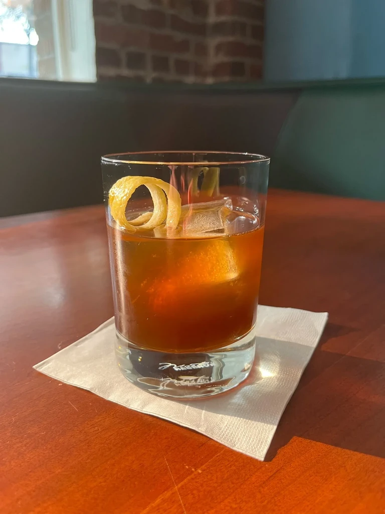 Amber cocktail with lemon peel and ice on a wooden table.
