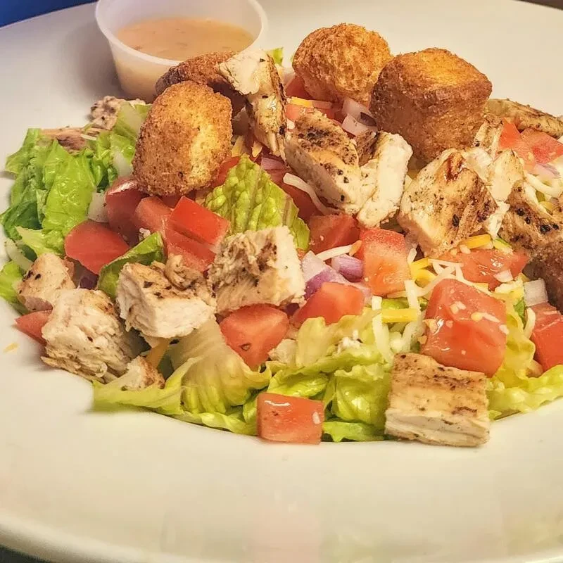 Salad with lettuce, tomatoes, grilled chicken, cheese, and fried items.