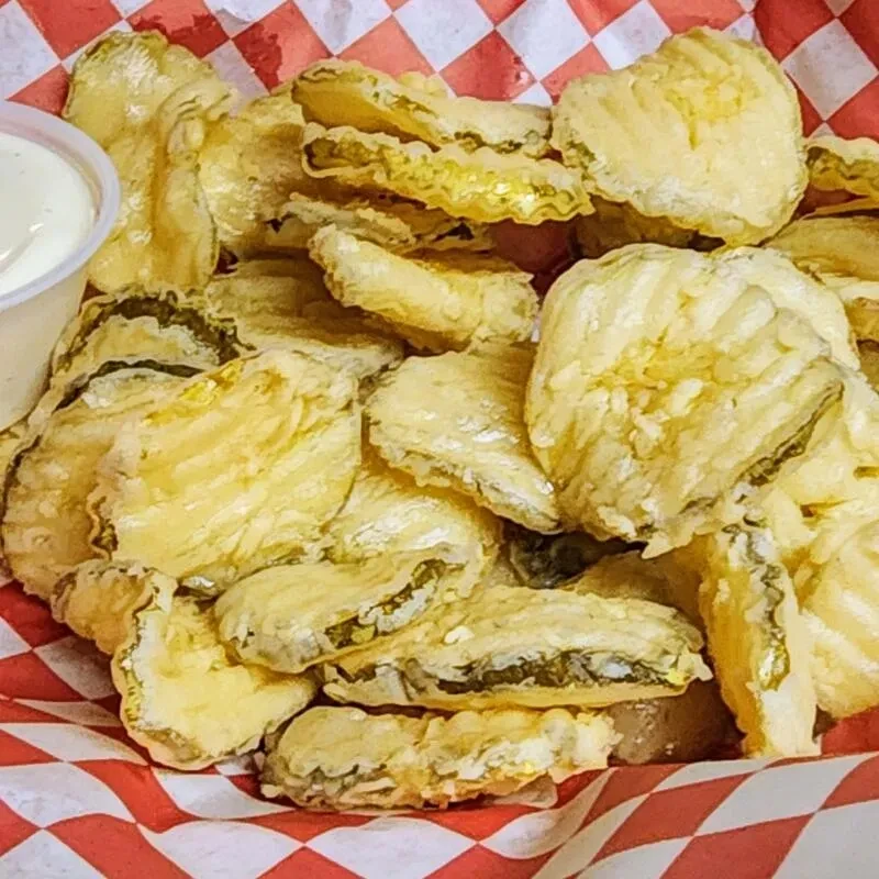Golden, crispy fried pickles with dipping sauce in a checkered basket.