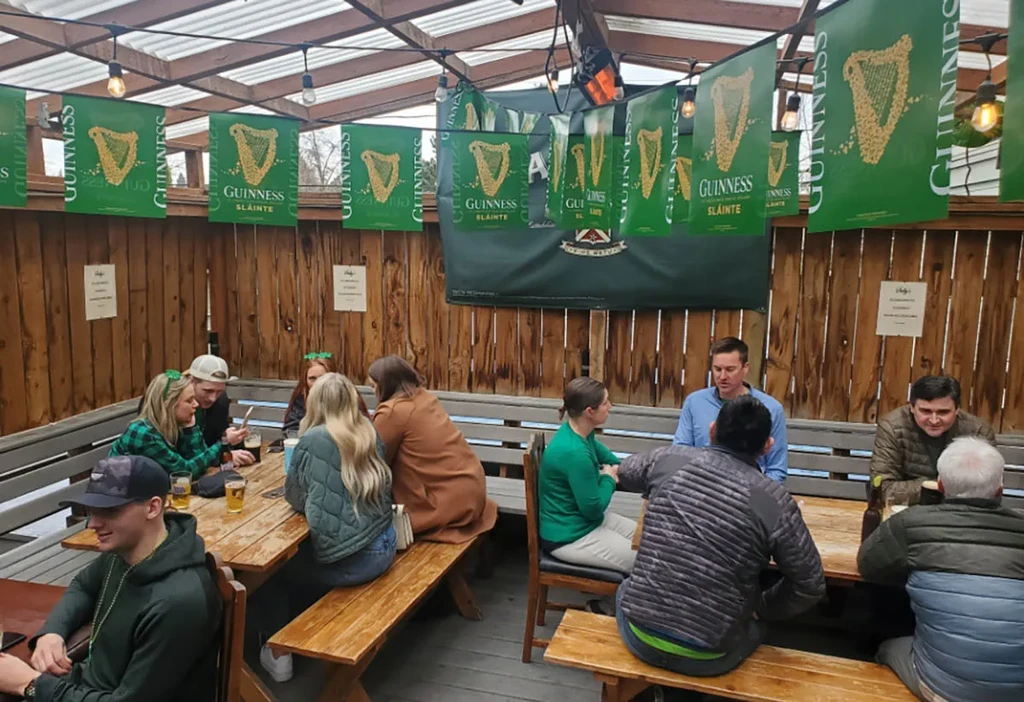 Rustic Irish pub patio with Guinness banners, people enjoying drinks.
