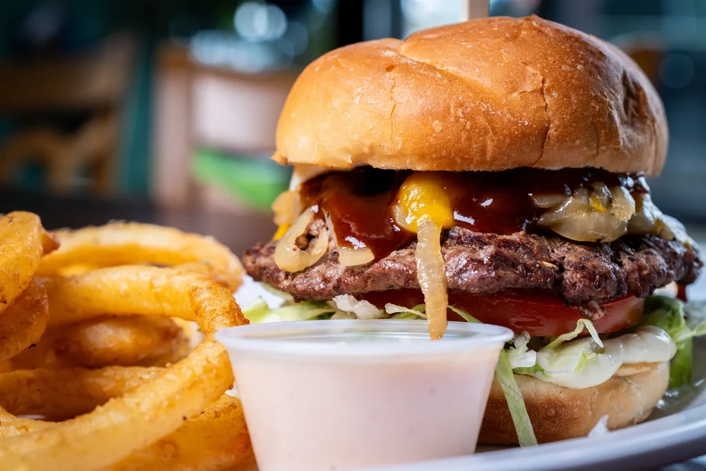 A close-up of a gourmet burger, golden onion rings, and dipping sauce.