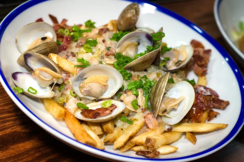 Close-up: steamed clams, creamy sauce, bacon, green onions, and fries.
