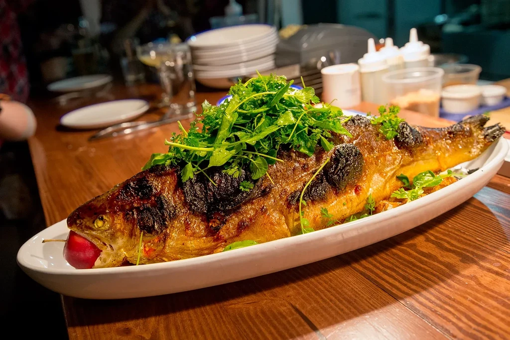 Golden-brown roasted fish with green herbs and a red cherry.