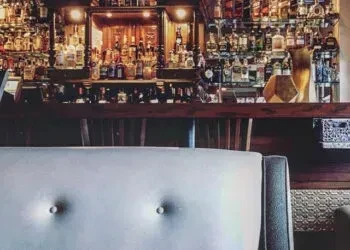 Well-stocked wooden bar counter with shelves of liquor bottles.