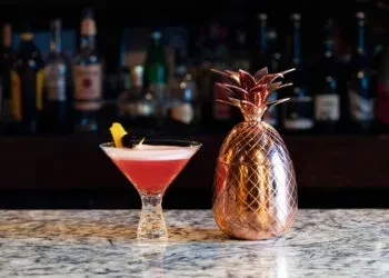 Pink martini, lemon twist, rose gold pineapple shaker on bar counter.
